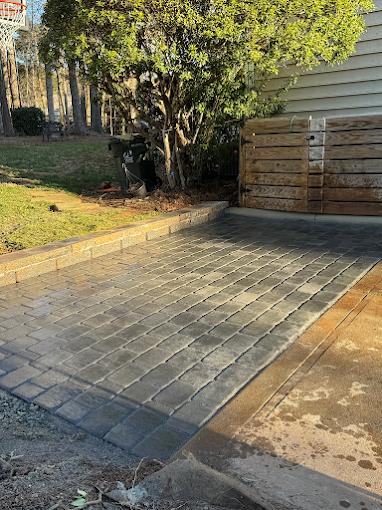 Paved driveway with brick edging, wooden gate, large tree, and residential house