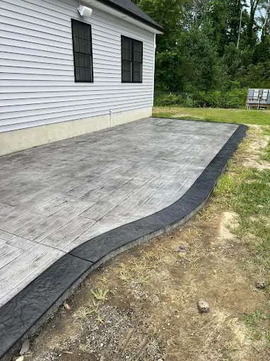 New concrete patio with dark border beside white house with black windows