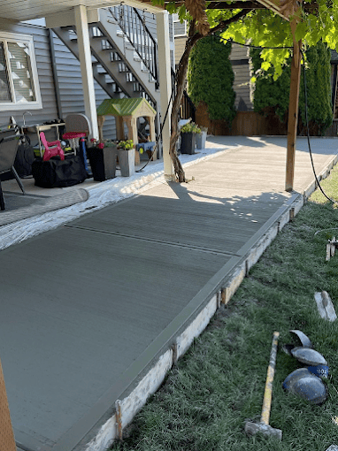 Freshly poured concrete walkway with ivy-covered posts beside residential house entrance