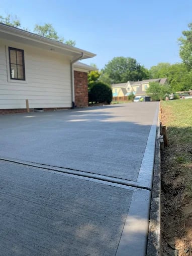 Concrete driveway beside white house with brick chimney and green trees
