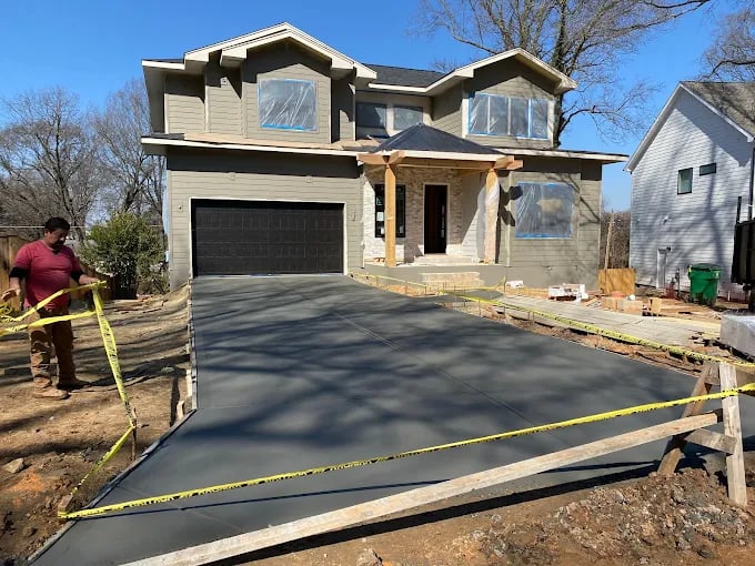 New two-story house with freshly poured concrete driveway under construction with yellow caution tape