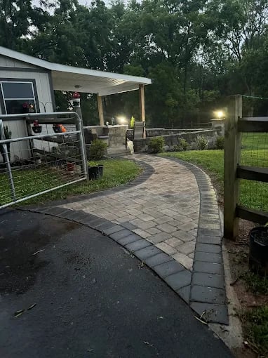 Outdoor patio area with wooden pergola, paver pathway, and landscaping at dusk.