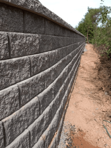 Concrete retaining wall along a dirt pathway with vegetation on the right side