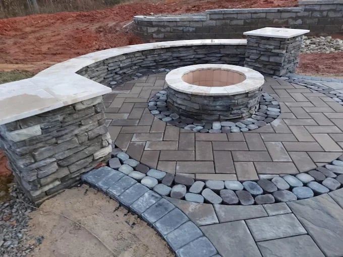 Stone patio with circular fire pit and bench seating under construction
