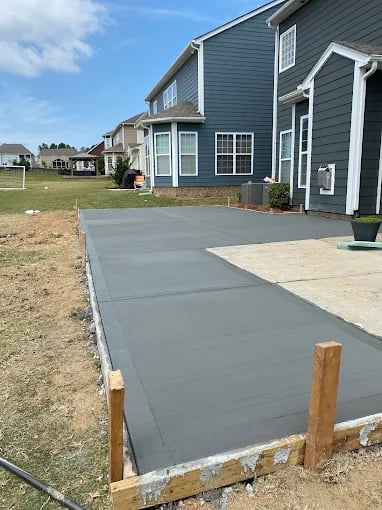 Dark blue two-story house with newly poured concrete driveway and wooden border framing