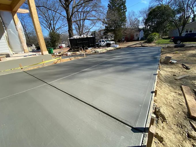 Freshly poured concrete foundation in residential driveway construction site with equipment and houses.