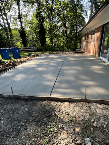 New concrete patio with trees and brick house in background