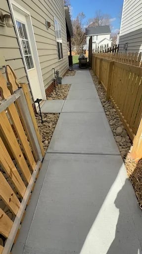 Narrow concrete walkway between wooden fences and residential houses with bare trees in background