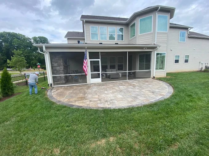 Modern two-story house with white siding, screened porch, curved patio, and American flag displayed.