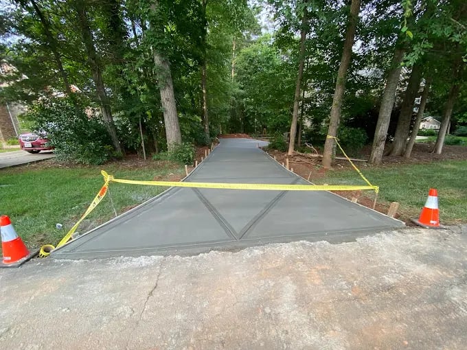 Newly poured asphalt driveway under construction, cordoned with yellow tape and traffic cones.